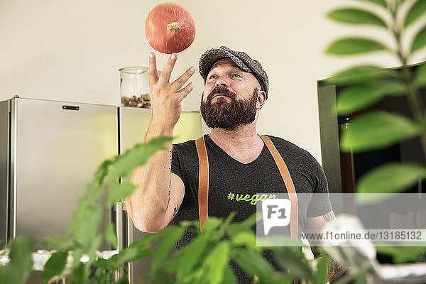 Veganer spielt mit einem Kürbis in seiner Küche