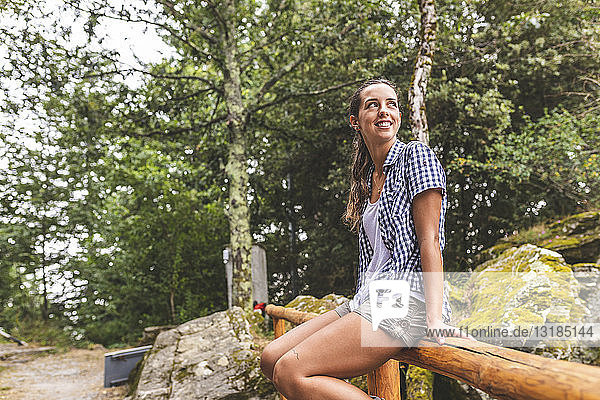 Italy  Massa  smiling young woman sitting on a wooden fence in the Alpi Apuane