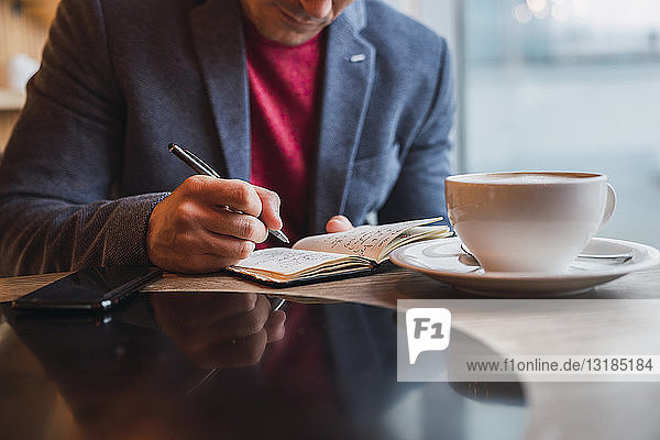 Geschäftsmann sitzt im Restaurant trinkt Kaffee und schaut in sein Notizbuch