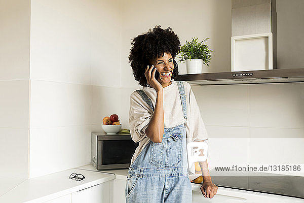 Lachende Frau am Handy in der Küche zu Hause