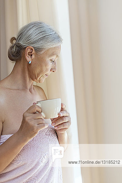 Ältere Frau in ein Handtuch gewickelt und trinkt morgens eine Tasse Kaffee