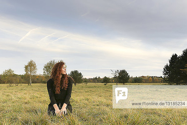 Redheaded young woman crouching on a meadow in autumn