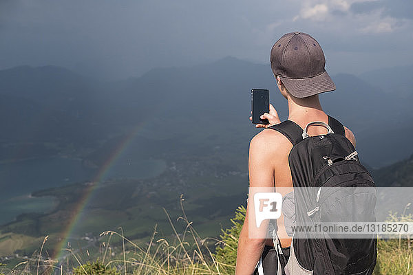 Österreich  Salzkammergut  Mondsee  Teenager beim Fotografieren eines Landschaftsbildes mit Regenbogen