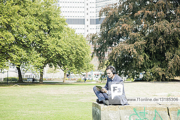 Businessman in city park wearing headphones and using tablet