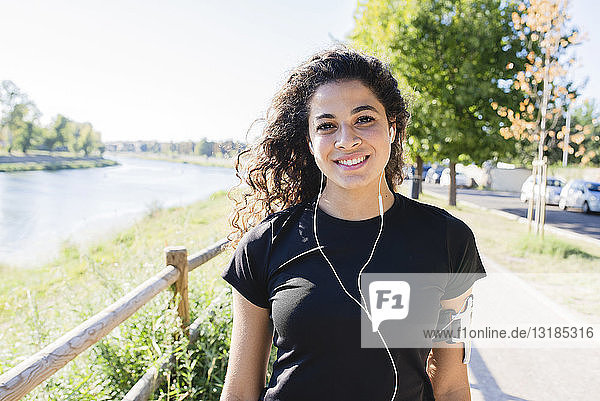 Porträt einer lächelnden  sportlichen jungen Frau am Flussufer