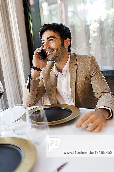 Lächelnder Mann sitzt am Tisch in einem Restaurant und telefoniert mit dem Handy