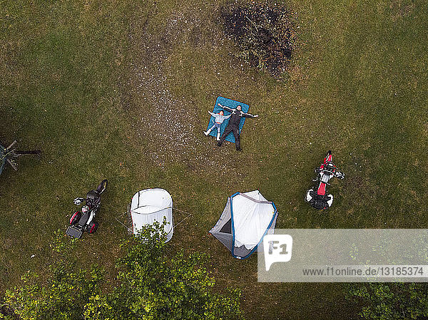 Father and son lying on a meadow next to tent and motorbike