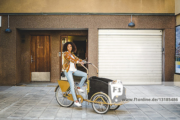 Mittlere erwachsene Frau in voller Länge auf Fahrradwagen mit Hund gegen Gebäude