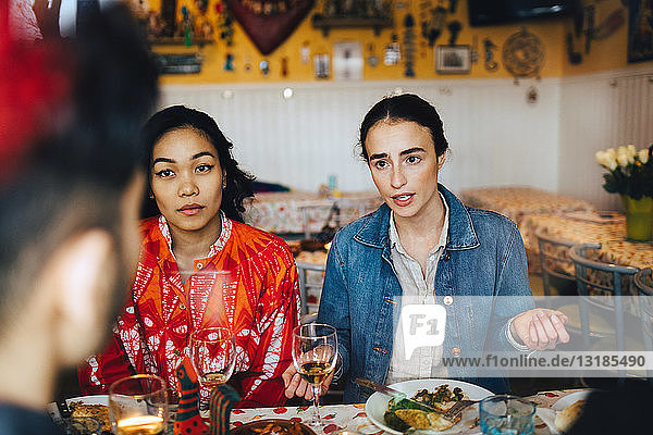 Junge Frauen im Gespräch mit einem männlichen Freund während einer Dinnerparty im Restaurant
