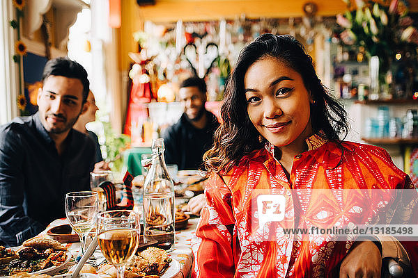 Porträt einer lächelnden jungen Frau  die am Tisch gegen multi-ethnische Freunde sitzt  die einen Brunch im Restaurant genießen