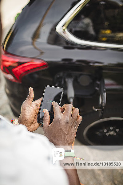 Ausgeschnittenes Bild eines Mannes  der ein Smartphone benutzt  während er im Auto auf der Einfahrt steht