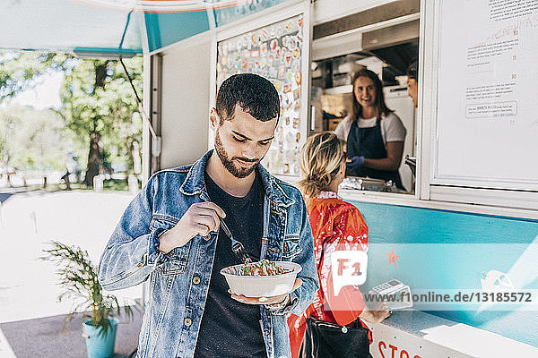 Young man eating fresh Tex-Mex in bowl against food truck