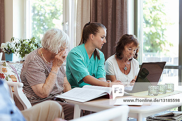 Beschäftigte im Gesundheitswesen und ältere Frauen mit Laptop und medizinischen Berichten im Pflegeheim