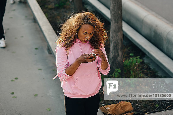 Schrägansicht einer Frau  die im Skateboard-Park Textnachrichten per Handy verschickt