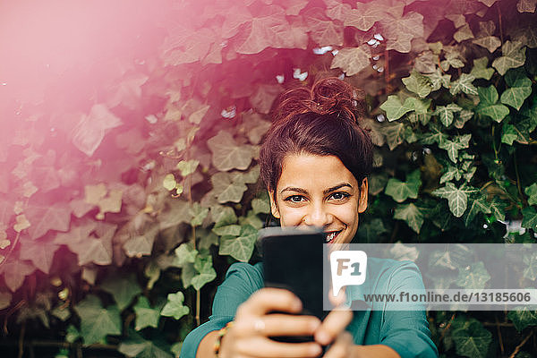 Portrait of smiling young woman photographing through mobile phone in backyard
