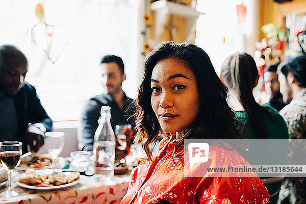Portrait of confident young woman sitting at table against multi-ethnic friends enjoying brunch in restaurant