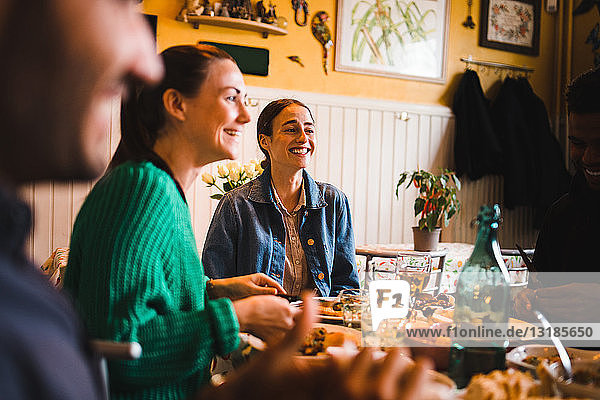Lächelnde junge Frauen sitzen im Restaurant am Tisch  während sie eine Dinnerparty genießen