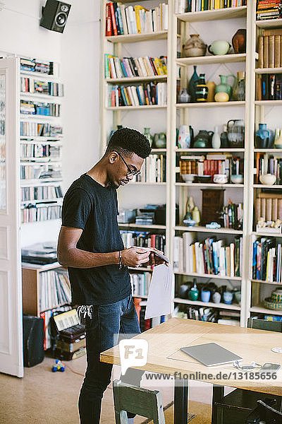Junger Mann liest Zeitung  während er zu Hause am Tisch steht