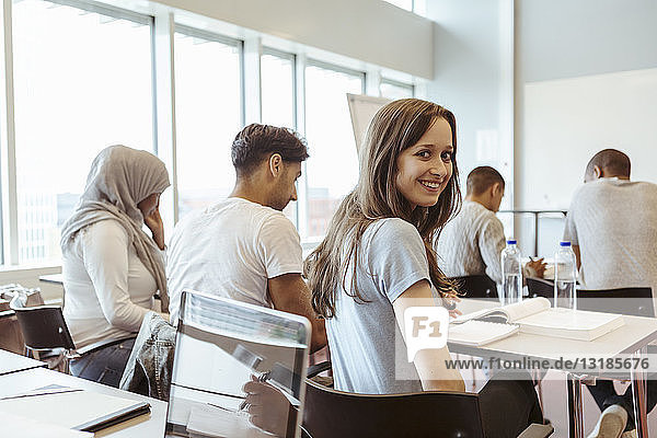 Portrait of smiling student sitting with friends in classroom at high school
