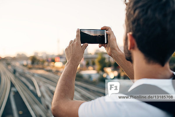 Junger Mann fotografiert per Smartphone über Eisenbahnschienen in der Stadt