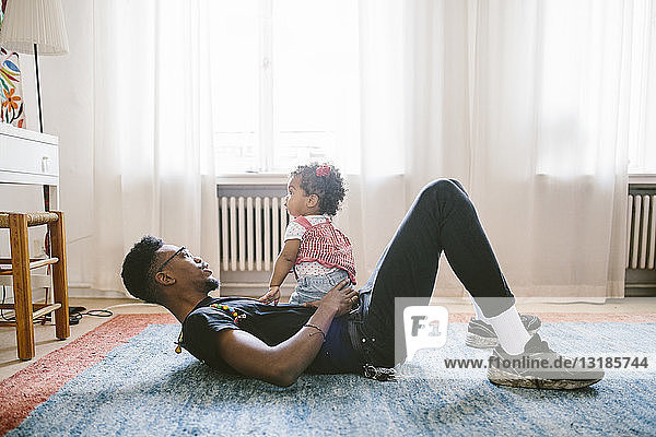 Kleines Mädchen sitzt auf dem zu Hause liegenden Vater