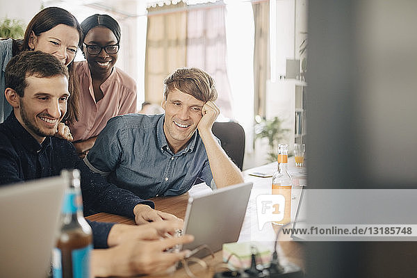 Lächelnde kreative Geschäftsleute  die während einer Besprechung im Büro auf ein digitales Tablet schauen