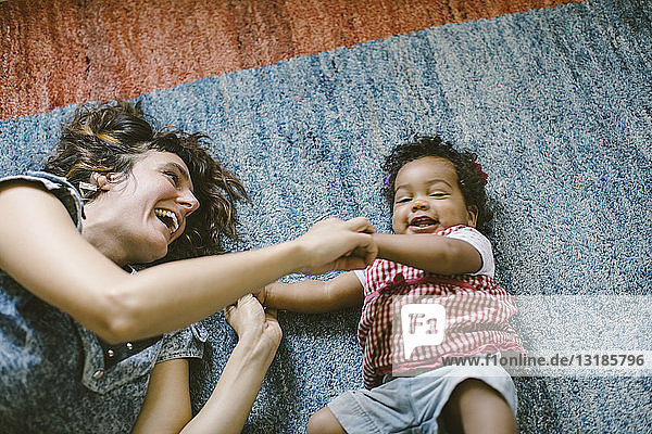 Hochwinkelansicht einer glücklichen Mutter und Tochter  die zu Hause auf dem Teppich liegen