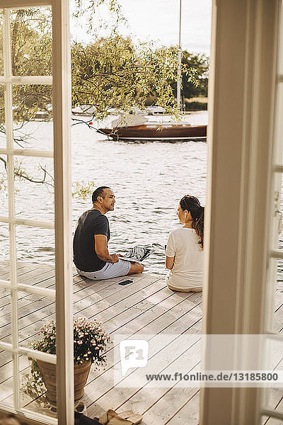 Mature couple talking while working at patio seen through open door of holiday villa