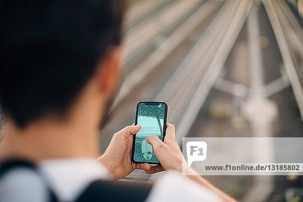 Ausgeschnittenes Bild eines jungen Mannes  der ein Smartphone über Eisenbahnschienen in der Stadt benutzt