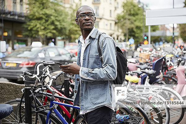 Mittlerer erwachsener Geschäftsmann schaut weg  während er in der Stadt an den Fahrrädern steht