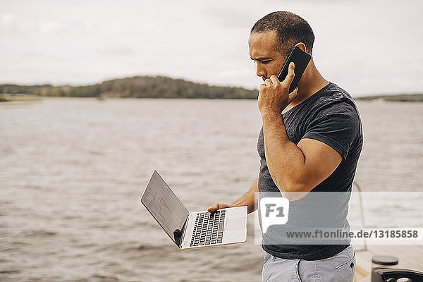 Erwachsener Mann telefoniert mit dem Laptop am See
