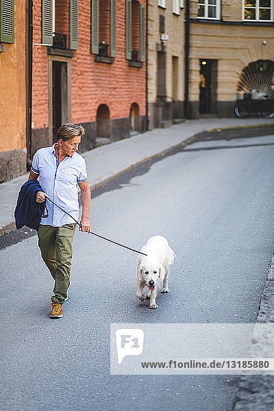 Älterer Mann geht in voller Länge mit Hund auf der Straße durch Gebäude in der Stadt