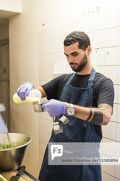 Selbstbewusster junger männlicher Koch gießt in der Großküche eines Restaurants Zutaten in einen Behälter