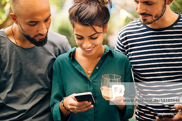 Lächelnde junge Frau zeigt männlichen Freunden ihr Handy  während sie im Freien steht