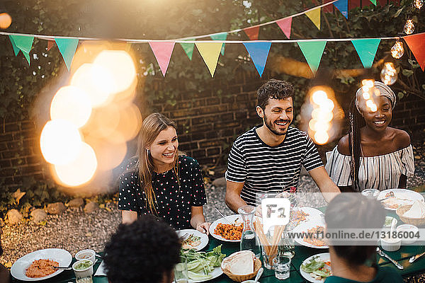 Glückliche multiethnische Freunde genießen das Abendessen am Tisch während der Gartenparty
