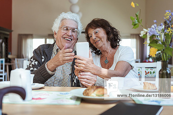 Senior couple taking selfie using mobile phone during breakfast at nursing home