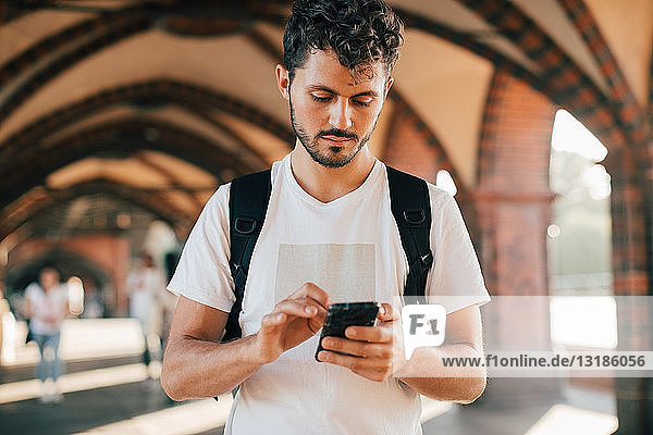 Junger Mann benutzt Smartphone  während er auf einem Fußweg steht
