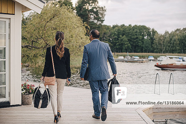 Rückansicht eines erwachsenen Paares beim Spaziergang an einer Ferienvilla am See