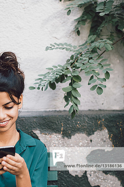 Cropped image of young woman using mobile phone against wall
