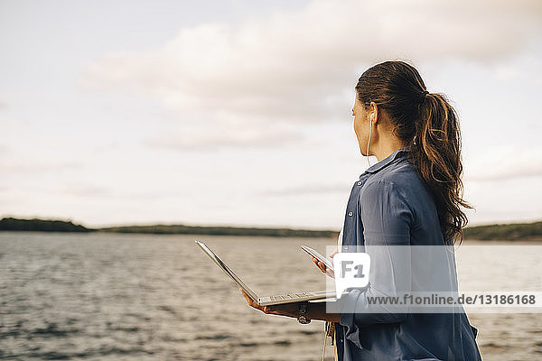 Eine reife Frau benutzt einen Laptop  während sie am See mit ihrem Handy telefoniert