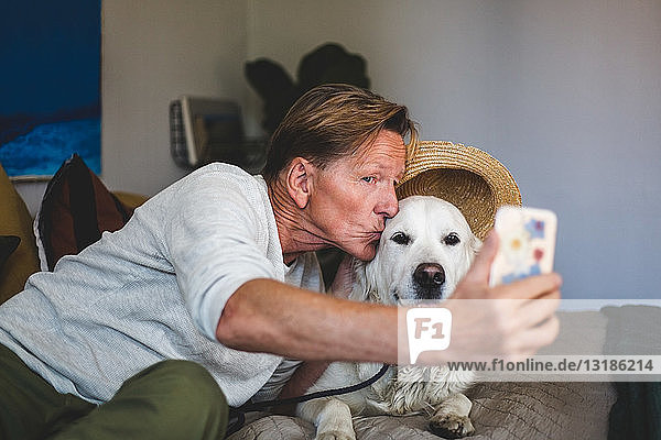 Älterer Mann küsst Hund  während er im Schlafzimmer zu Hause mit einem Smartphone Selbstgespräche führt