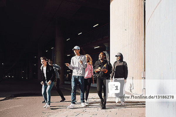 Glückliche Freunde schauen weg  wenn sie an einem sonnigen Tag auf der Straße unter der Unterführung in der Stadt spazieren gehen