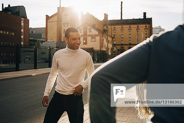 Lächelnder junger Mann genießt mit Freunden auf dem Bürgersteig in der Stadt an einem sonnigen Tag