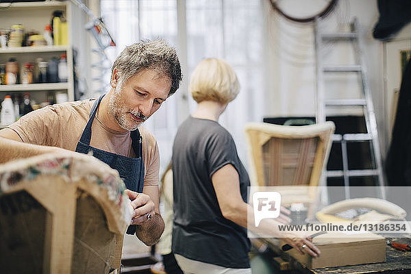 Mature craftsperson stitching sofa in workshop