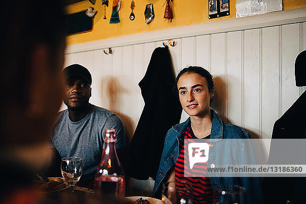 Junge Frau sitzt neben einem Mann  während sie während einer Dinnerparty eine Freundin im Restaurant anschaut