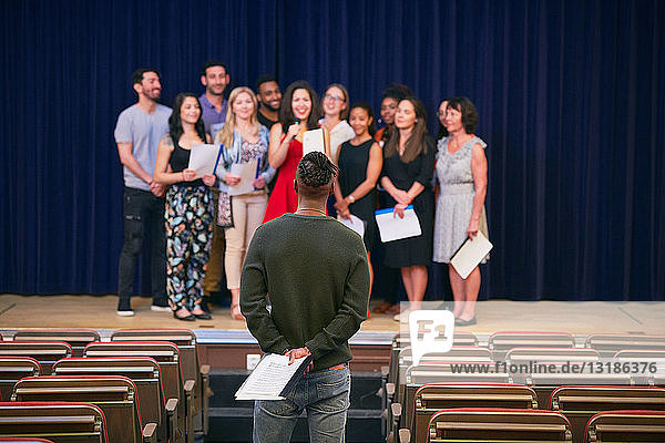 Musical teacher listening to choir on stage in auditorium of language school