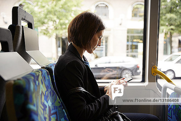 Seitenansicht einer Geschäftsfrau  die ein Smartphone benutzt  während sie im Bus sitzt