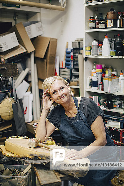 Portrait of confident female upholstery worker sitting at workbench in workshop