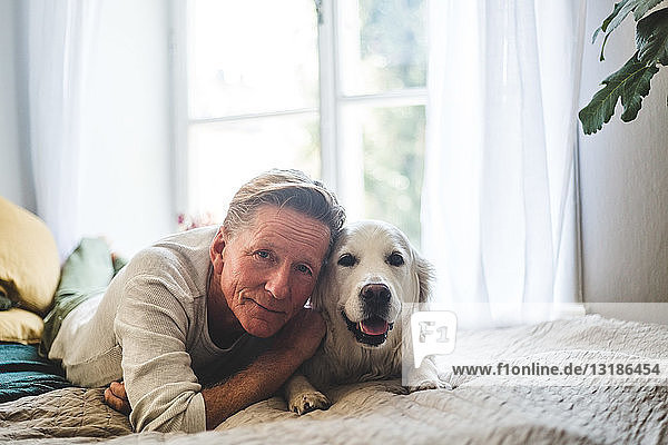Close-up portrait of senior man and dog lying on bed at home