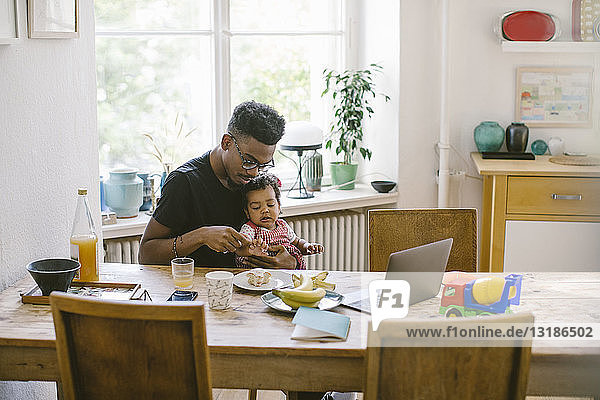 Young man playing with daughter while sitting at table in house